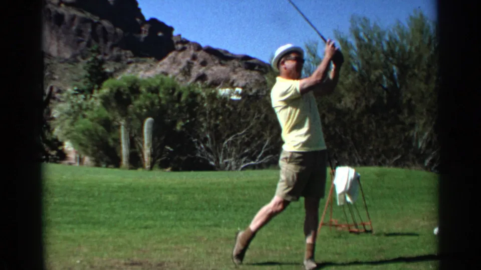 The golfer holds the finish of his swing on a Scottsdale fairway, with desert shrubs, cacti, and rocky hills in view.