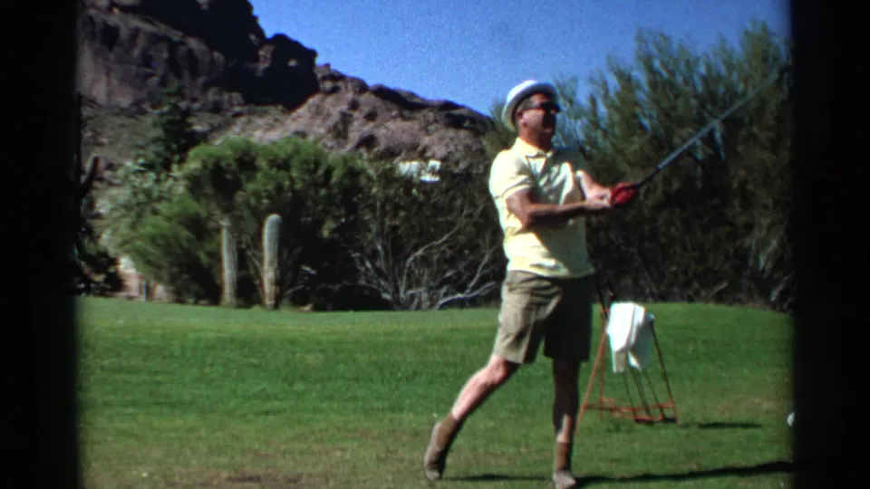 After the swing, the golfer lowers his club on the Scottsdale course while a towel stand, fairway, cacti, and hillside remain visible.