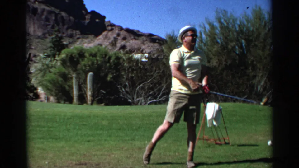 The golfer stands at the end of the motion on a Scottsdale desert fairway, with the club lowered and a towel stand behind him.