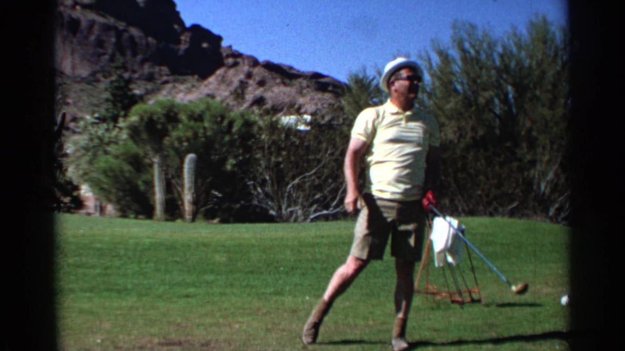 Man on sunny golf course with pull cart while woman prepares nearby.