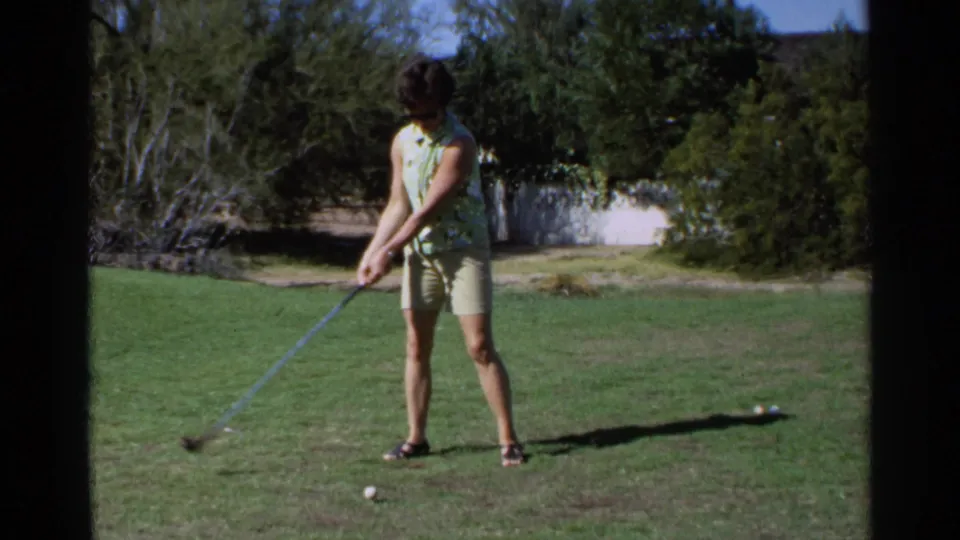 1968 Scottsdale frame of a woman in a green sleeveless shirt and shorts setting up a golf swing on a sunny course.