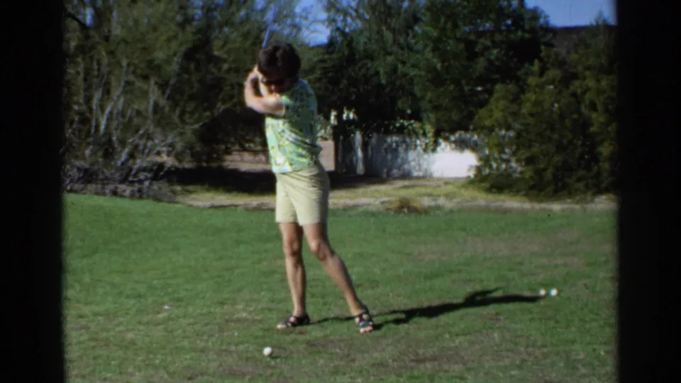 1968 Scottsdale home-movie frame showing the woman mid follow-through after striking or swinging at the golf ball.