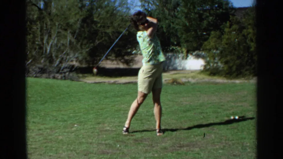 A woman golfer in sunglasses finishes a swing in the 1968 Scottsdale 8mm home-movie scene.