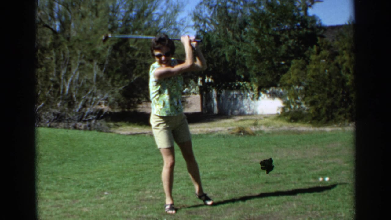 Woman on a lawn holding a golf club at the top of a backswing.