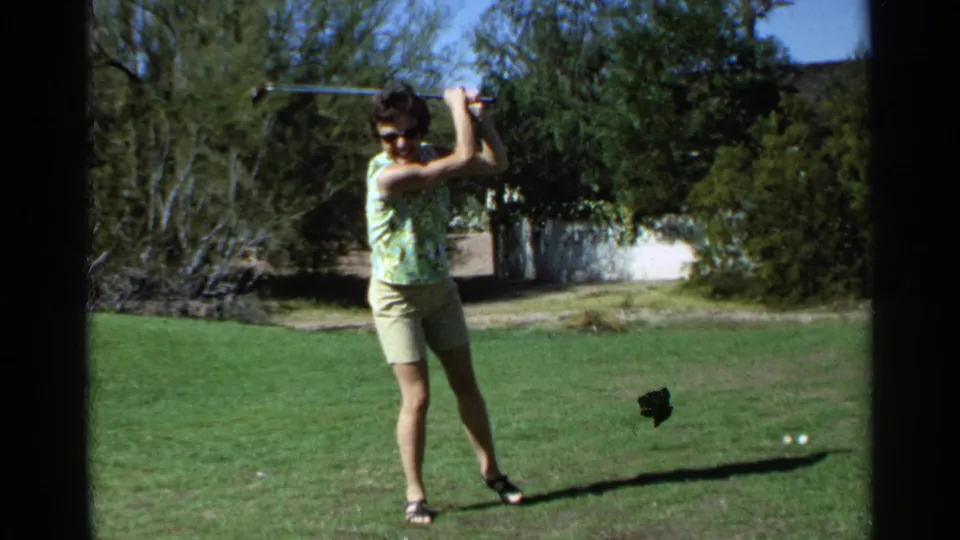Adult woman in Scottsdale, Arizona, 1968, stands on grass with a golf club raised during a backyard swing practice.