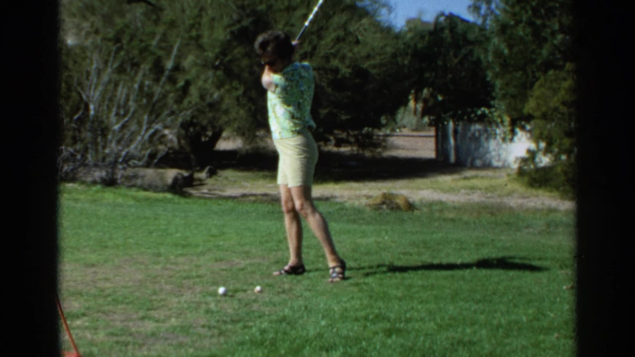 Woman golfer follows through on a swing on a sunny grass course.