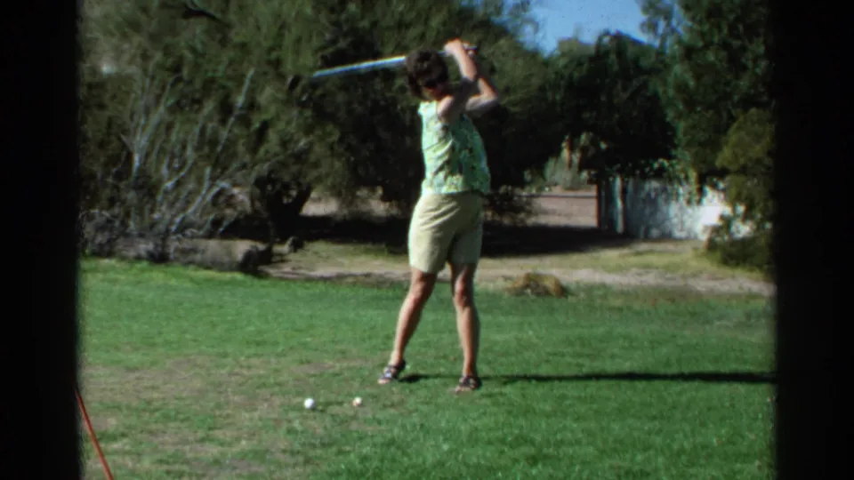 A woman in light shorts raises her club into a backswing on a sunny Scottsdale golf course in metadata-supported 1968 home-movie footage.