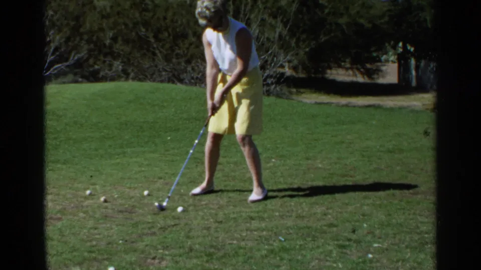 A second woman in a white sleeveless top and yellow skirt lines up a putt on a Scottsdale golf course in 1968 footage.