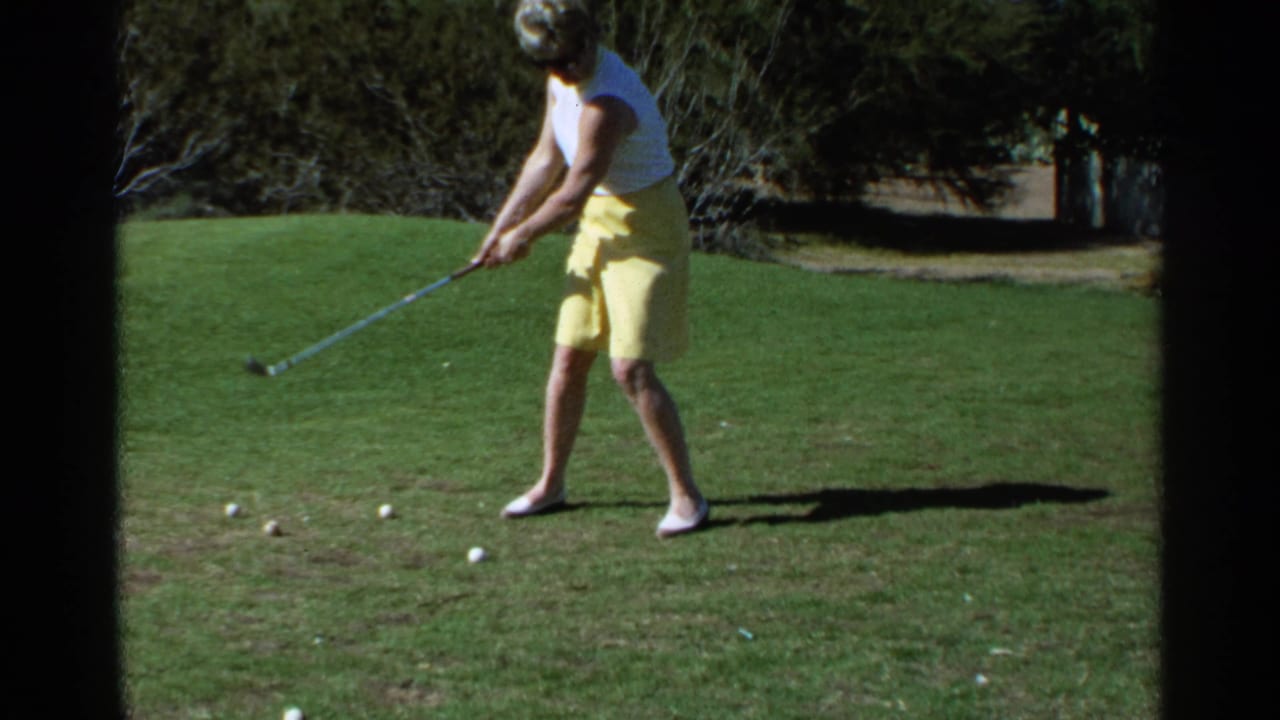 Woman in yellow skirt addresses a golf ball on a sunny grass green.