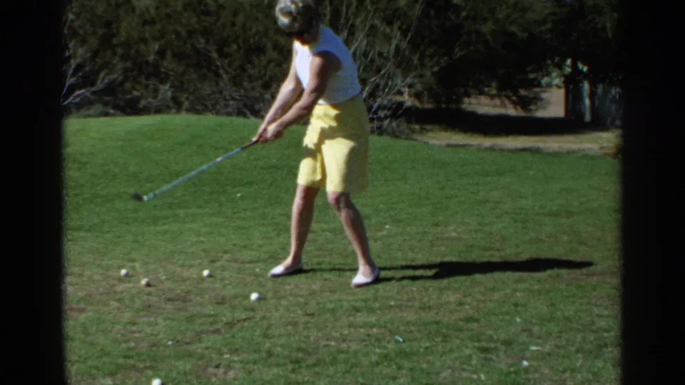 In Scottsdale, Arizona, 1968, a woman in a yellow skirt and white sleeveless top begins a golf swing on a sunlit green.