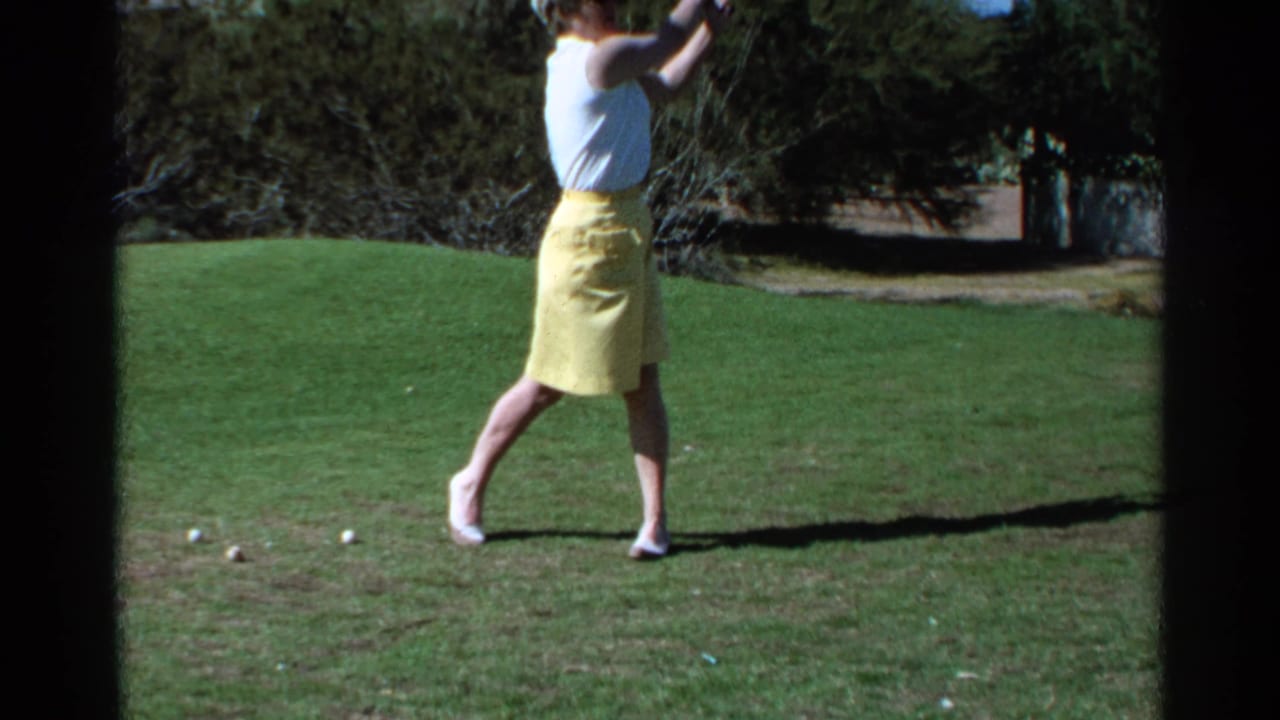 Woman in a white sleeveless top and yellow skirt raises a golf club on a sunny grass course.