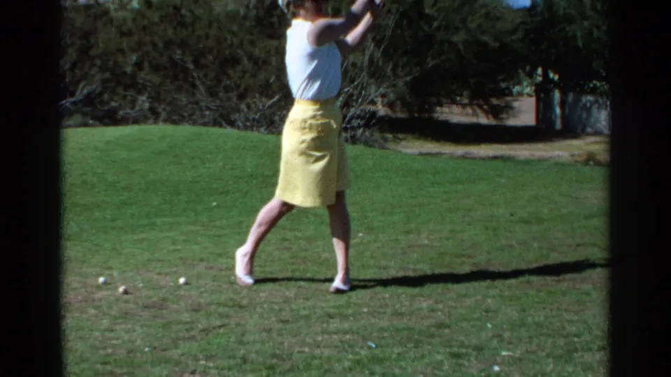 In Scottsdale, Arizona, 1968, a woman golfer in a white sleeveless top and yellow skirt lifts her club on a sunlit course.