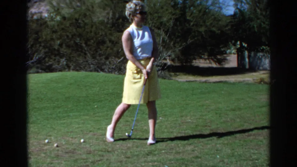 The woman golfer stands with her club near a ball on the Scottsdale grass, framed by trees in the 1968 8mm home-movie footage.