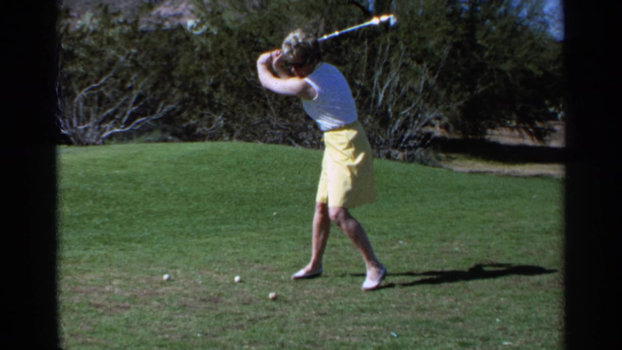 In the 1968 Scottsdale golf scene, the woman reaches the top of her backswing with golf balls on the grass in front of her.
