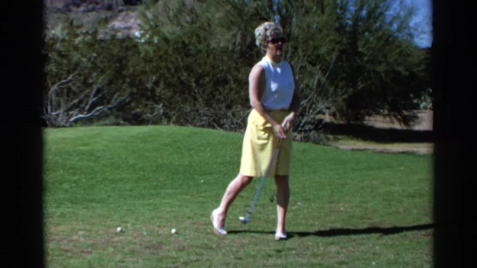 A woman in 1968 Scottsdale stands with a golf club on a bright lawn, with desert vegetation in the background.