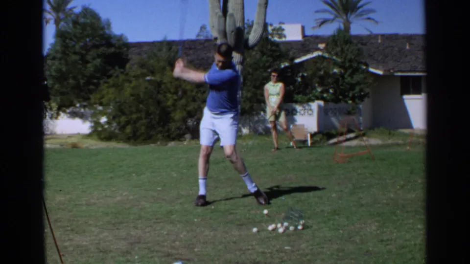 In Scottsdale, Arizona, 1968 home-movie footage, a man starts a golf swing on a backyard lawn as a woman watches near shrubs and a house.