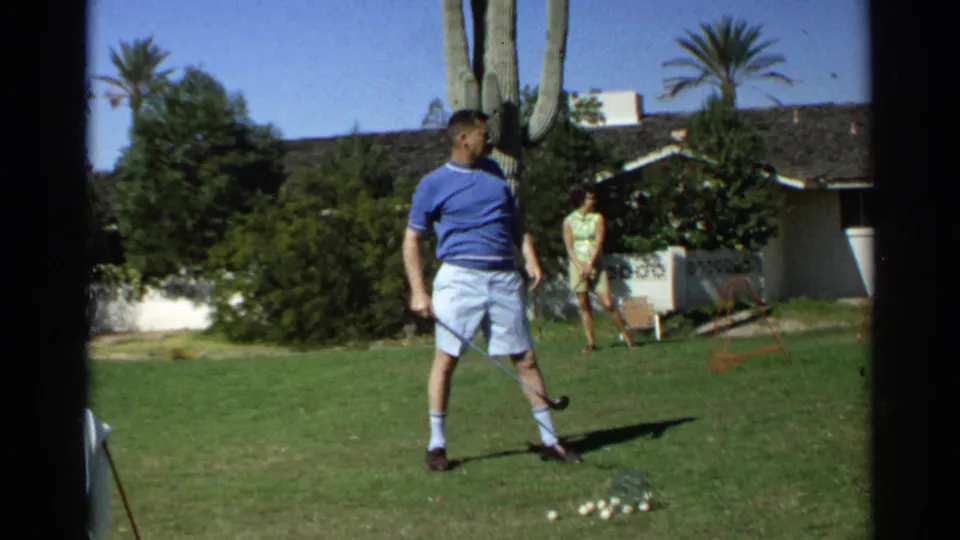 A 1968 Scottsdale backyard scene shows a man holding a golf club near a cluster of balls while a woman stands by the house in the background.