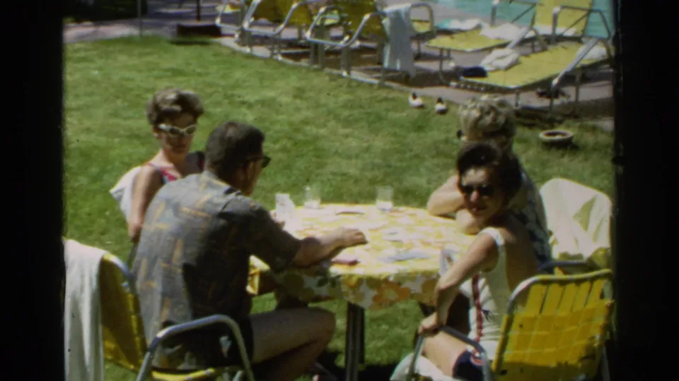 1968 Scottsdale frame showing adults around a picnic table on a lawn, with swimwear, sunglasses, and poolside seating visible.