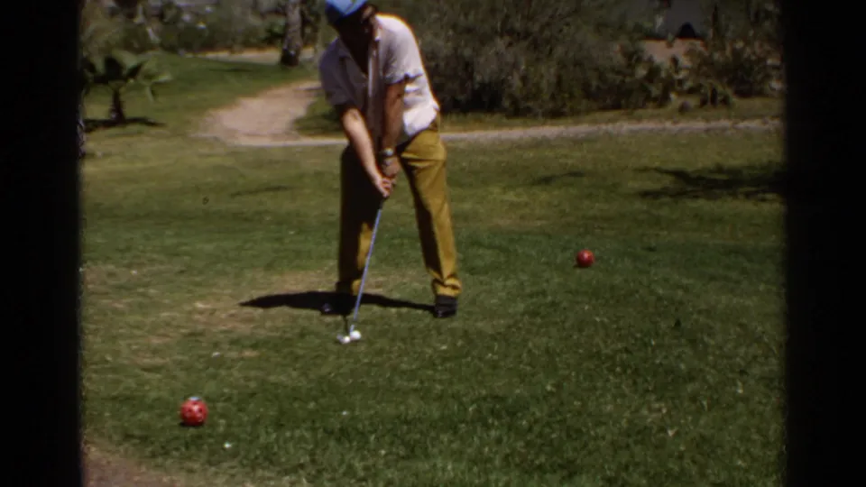 1968 Scottsdale home-movie frame of a man in a white shirt and yellow pants preparing to putt on a lawn or green.