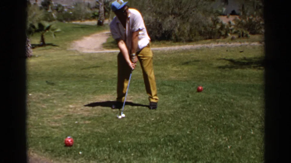 1968 Scottsdale frame of a casual golfer preparing a putt on grass, framed with soft 8mm exposure and visible lawn texture.