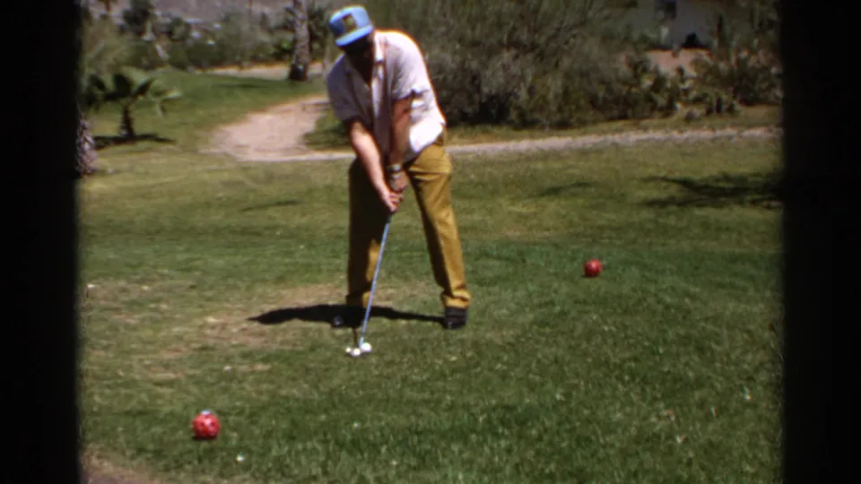 In 1968 Scottsdale footage, a man in a white shirt and yellow trousers prepares to swing a golf club on a sunny fairway.