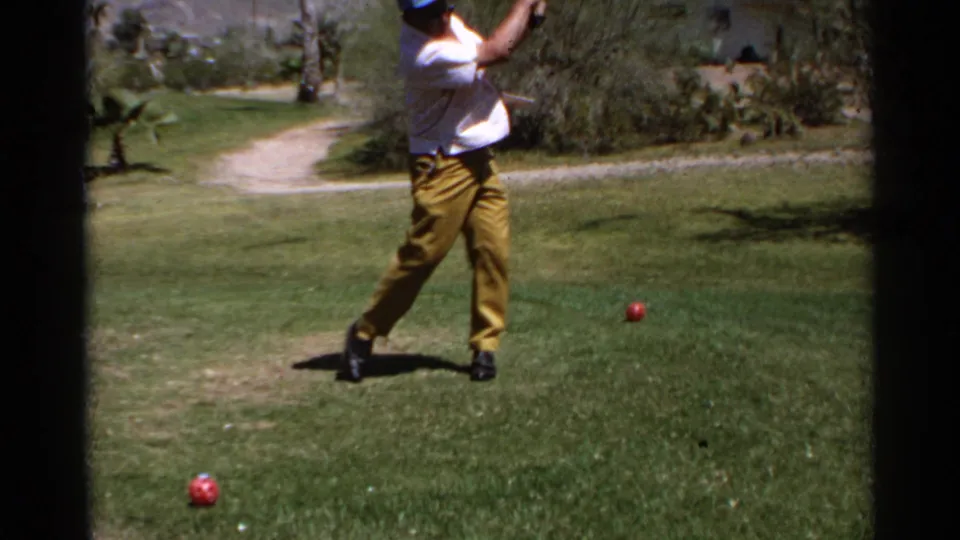 The golfer completes his follow-through on the sunlit Scottsdale fairway, with red balls and desert landscaping still visible around him.