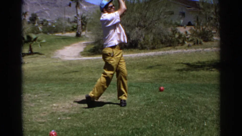 A man on a Scottsdale golf course in 1968 holds his follow-through while a red ball sits on the grass near desert plants and palms.