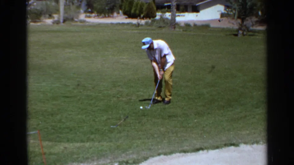 Golfer prepares a putt or short shot on a green in the supplied 1968 Scottsdale home-movie footage.