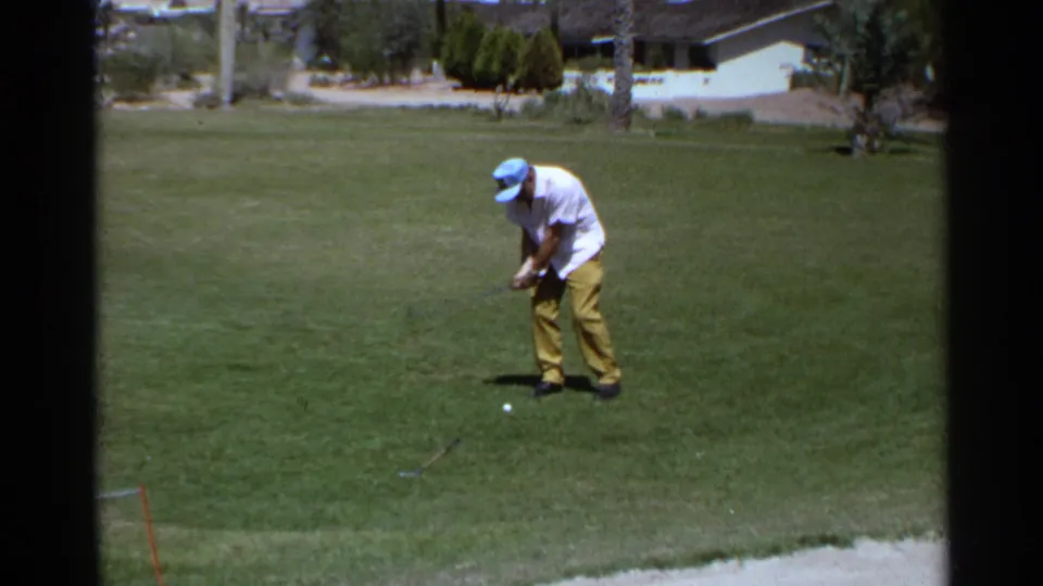 Adult golfer on a 1968 Scottsdale course prepares his swing, framed by 8mm borders and a sunlit suburban backdrop.