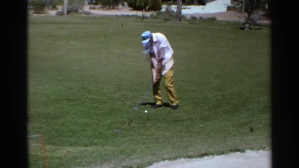 A 1968 Scottsdale golf practice moment shows the golfer moving through his swing on a green bordered by sand and distant houses.