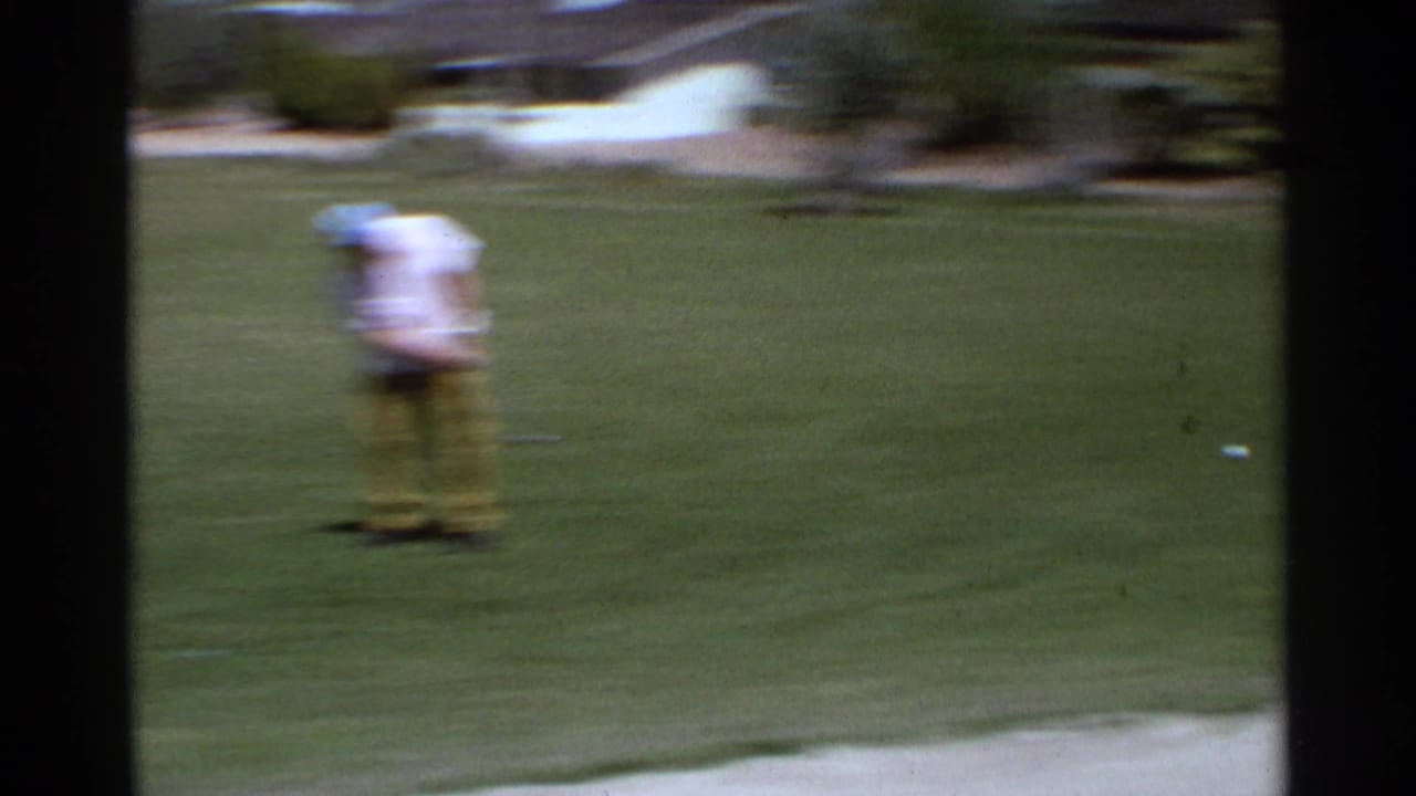 A man in light shirt and yellow pants appears blurred while standing on a Scottsdale golf green in 1968 home-movie footage.