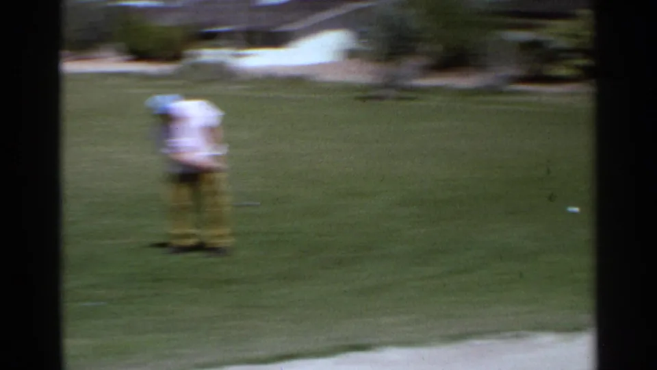 A man in light shirt and yellow pants appears blurred while standing on a Scottsdale golf green in 1968 home-movie footage.