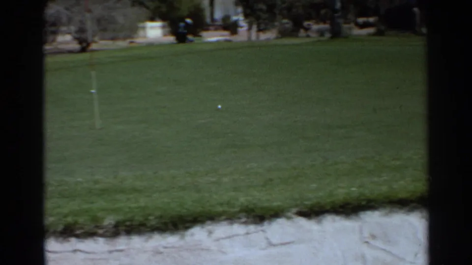 A Scottsdale golf course green shows a flagstick, ball, sand trap edge, and trees in 1968 8mm footage.