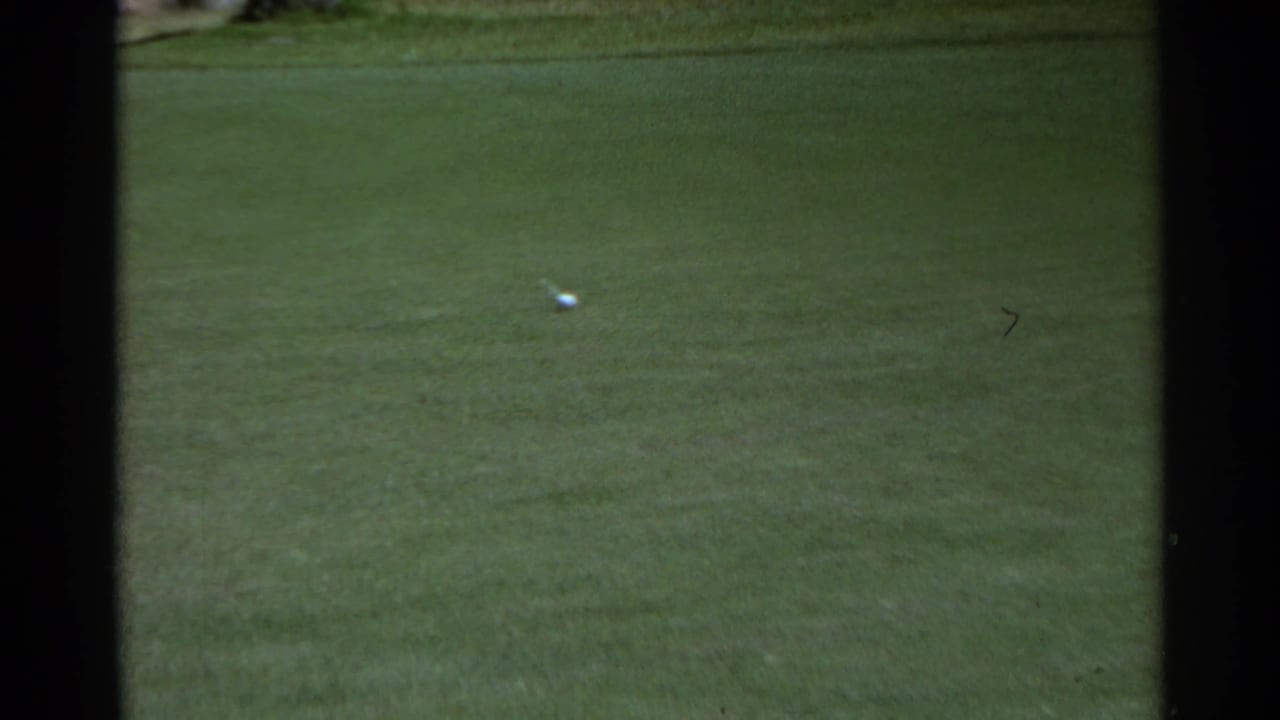 A golf ball rests on a wide green in the Scottsdale course scene, with soft 8mm color and minimal background detail.