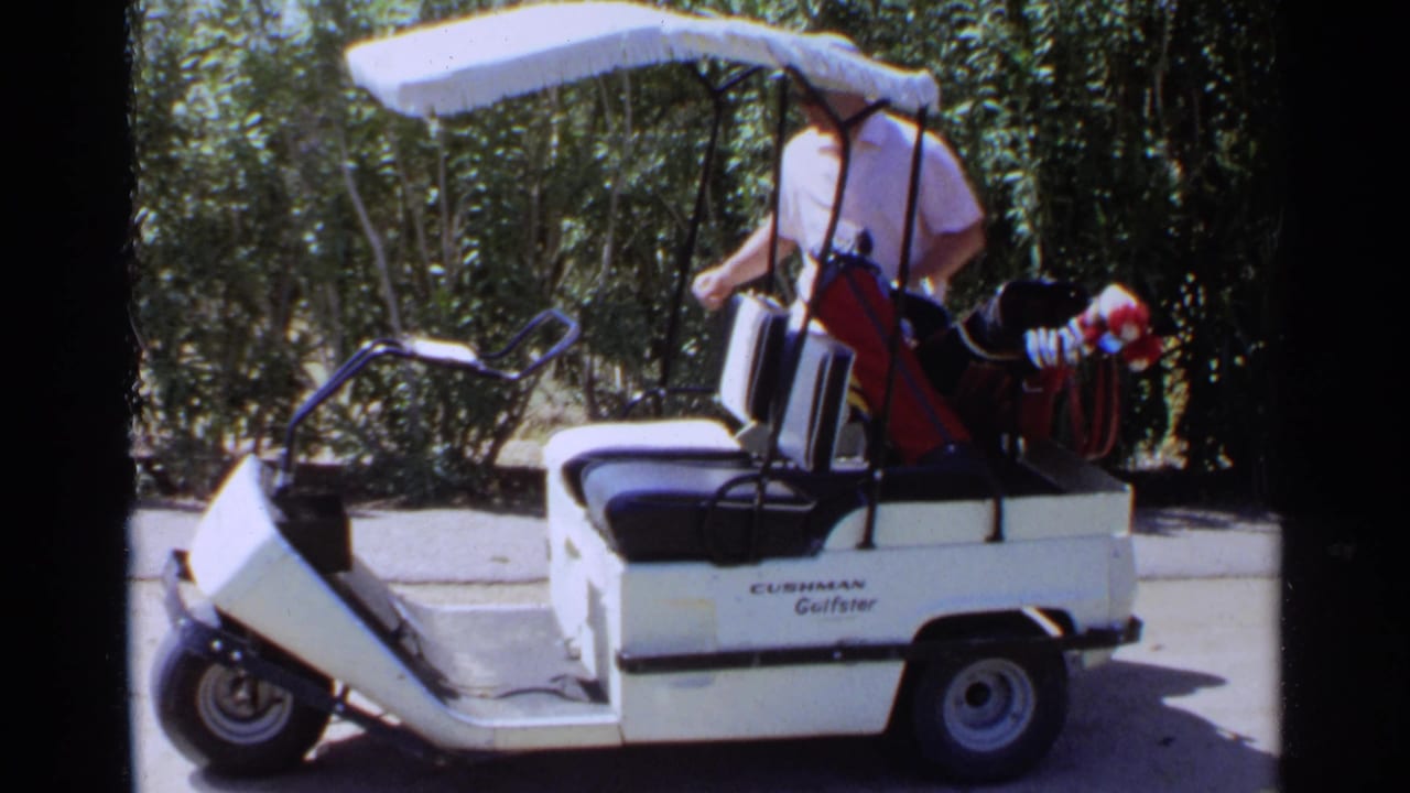 Man standing beside a white golf cart with a golf bag and clubs.