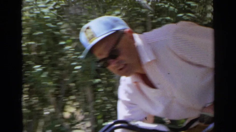 A close, slightly blurred home-movie frame shows the man leaning forward near the cart in Scottsdale, Arizona, in 1968.
