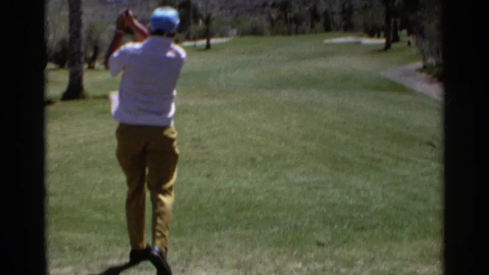 Older golfer follows through after a swing on a sunlit Scottsdale fairway in 1968 8mm home-movie footage.