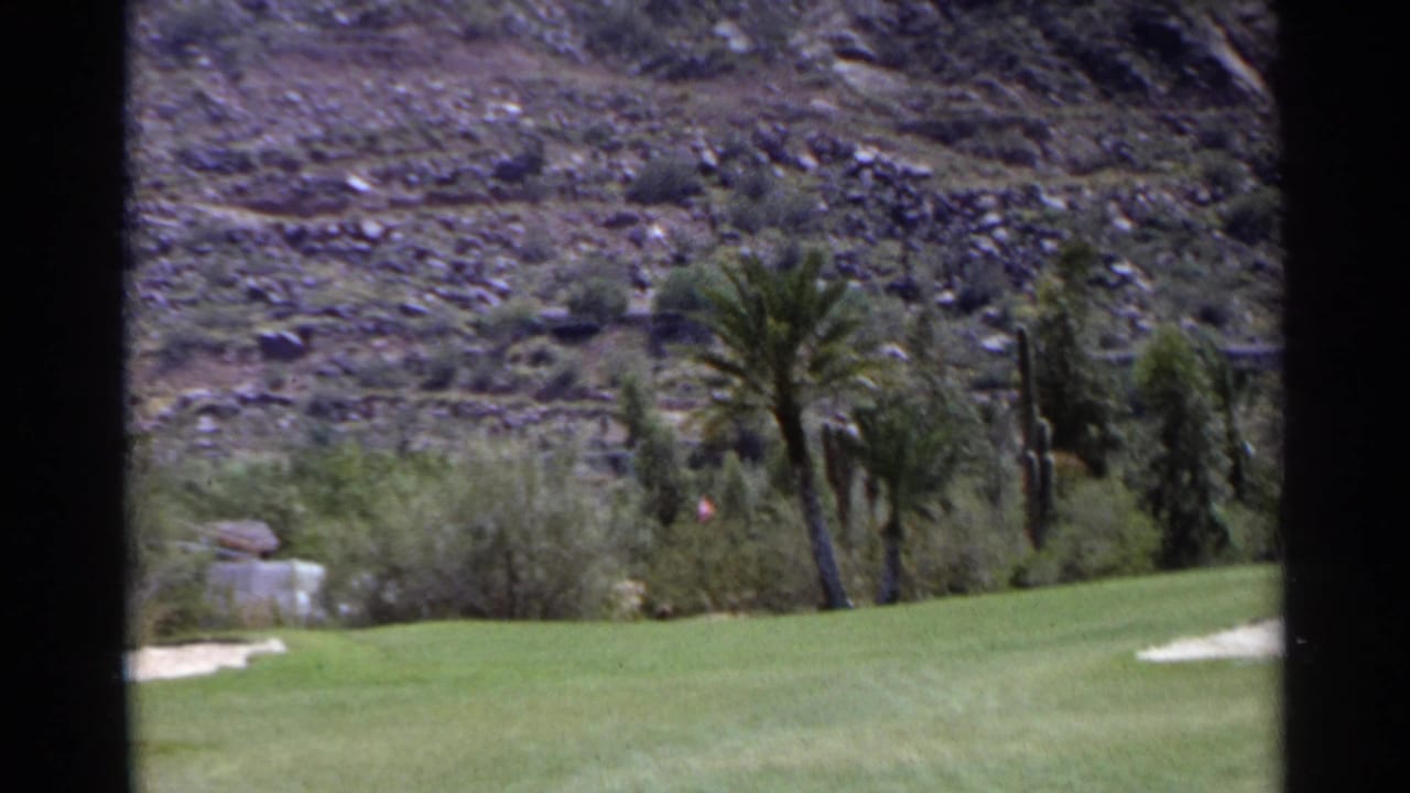 1968 Scottsdale golf course view with green fairway, palms, sand trap, shrubs, and rocky desert hillside.