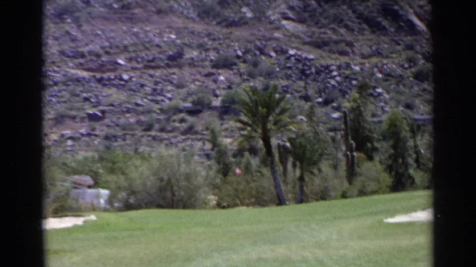 1968 Scottsdale golf course view with green fairway, palms, sand trap, shrubs, and rocky desert hillside.