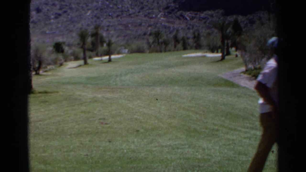 1968 Scottsdale home-movie frame showing a palm-lined golf course, desert hills, and a golfer partly cut off at the right edge.