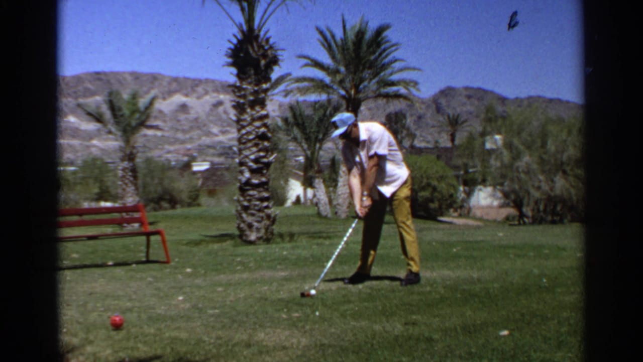 Adult golfer on a 1968 Scottsdale course stands over the ball, with palms, green grass, and desert hills visible behind him.