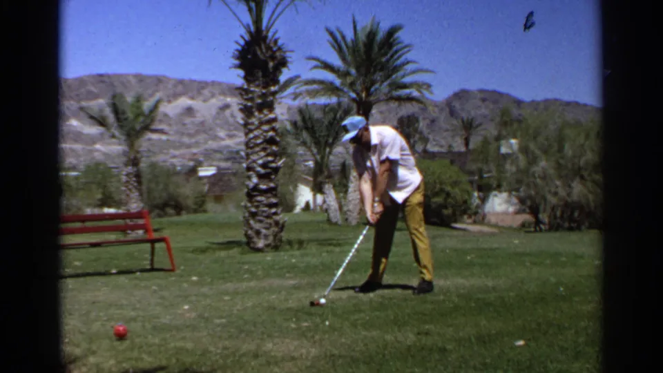 Adult golfer on a 1968 Scottsdale course stands over the ball, with palms, green grass, and desert hills visible behind him.