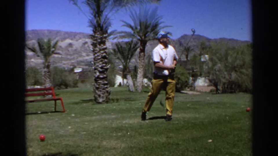In supported 1968 Scottsdale footage, a man in a white shirt and yellow trousers stands on a golf course with palm trees and mountains behind him.