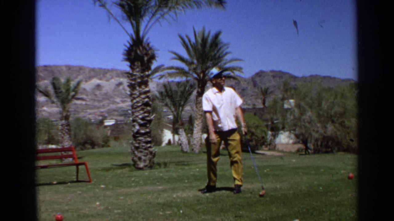 The golfer pauses over the ball on a sunny Scottsdale course, with palms, grass, and arid mountains visible in the background.