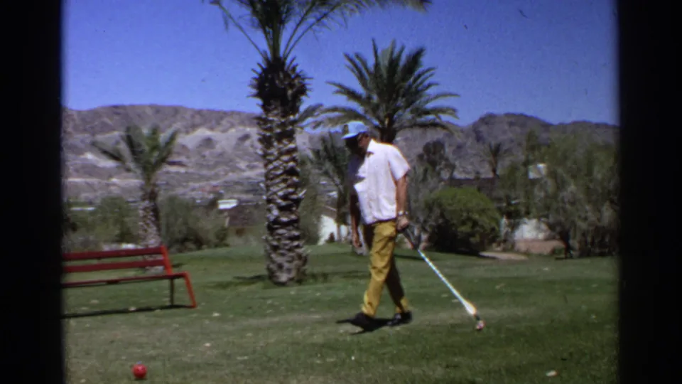 The man steps across the grass beside a golf ball, holding his club on a bright Scottsdale course in the supplied 1968 home-movie footage.