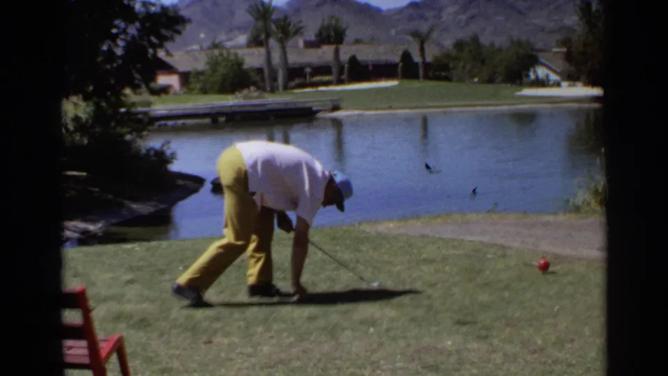 The adult golfer is bent forward on a Scottsdale course, framed by the pond, green lawn, palms, and desert mountains.