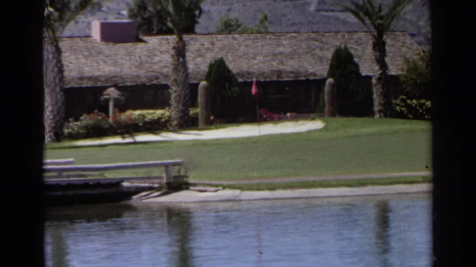 Scottsdale golf-course view with pond water, manicured grass, palm trees, low resort structures, and desert mountains in the background.