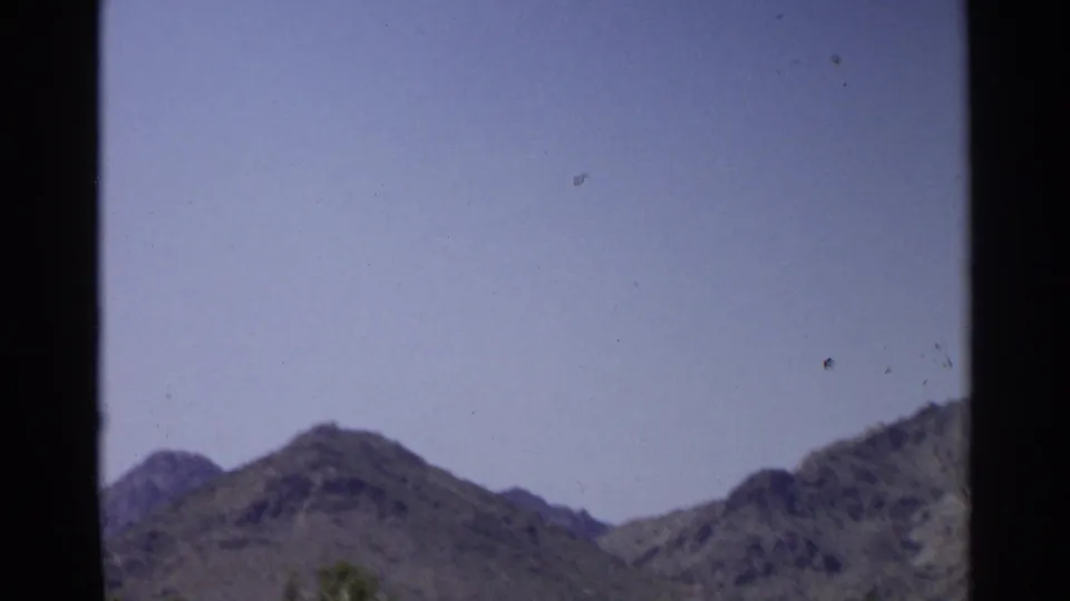 1968 Scottsdale home-movie frame showing hazy sky and desert mountains before the golf-course view appears.