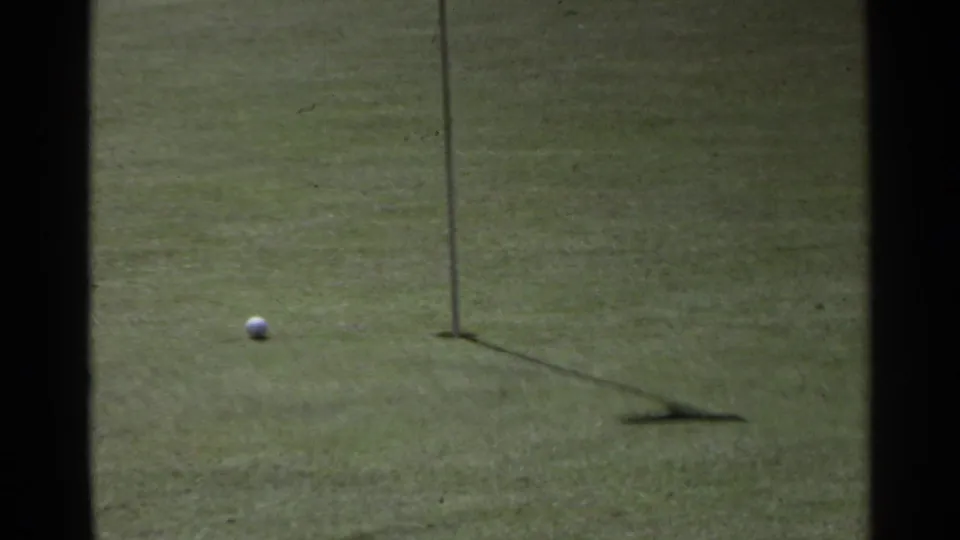 A golf ball rests near the shadow of a flagstick on a sunny putting green in 1968 Scottsdale footage.