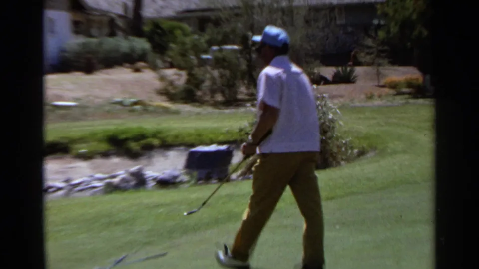 1968 Scottsdale home-movie frame showing a man in golf clothes walking across a course near desert landscaping.
